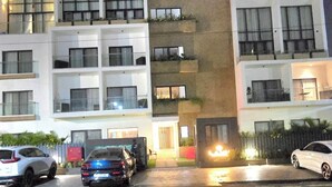 Hotel de vários andares com varandas, um elemento de destaque luminoso e carros estacionados.