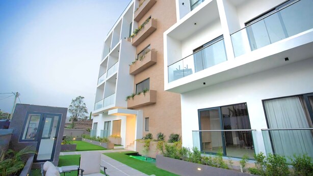 Um edifício residencial de vários andares com varandas, uma pequena área ajardinada e um design arquitetônico moderno.