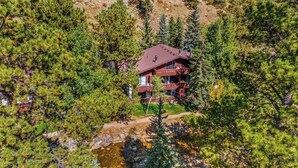 A cabin surrounded by dense pine trees, with a clear view of the surrounding forest. - Rocky’s Riverside Retreat - heated pool, river access (Estes Park)