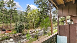 A wooden deck overlooking a rocky stream with trees, a small shed, and a house in the background. - Rocky’s Riverside Retreat - heated pool, river access (Estes Park)
