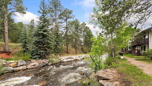 A river flowing through a forest with a lodge on the right. - Rocky’s Riverside Retreat - heated pool, river access (Estes Park)