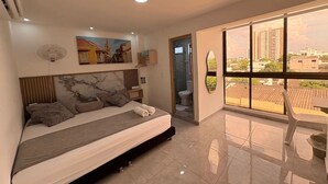 A modern bedroom with a large bed, a bathroom with a glass door, and a balcony with a city view. - HOTEL LA ESTRELLA DE DAVID  (Cartagena)