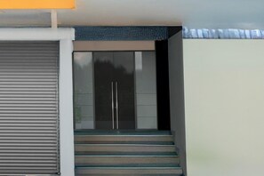 A set of stairs leading to a door with a glass panel, a closed roller shutter, and a textured wall above. - Deluxecollection O Kothapet (Hyderabad)