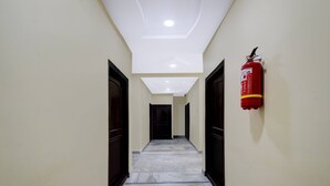 A hallway with a fire extinguisher mounted on the wall, a ceiling with recessed lighting, and a door at the end. - Deluxecollection O Kothapet Near Omini Hospital (Hyderabad)