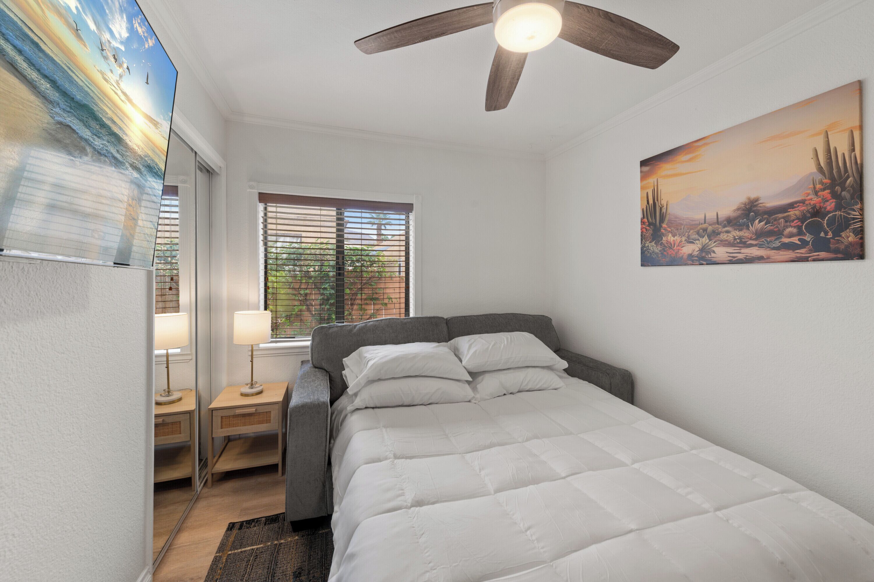 A bedroom with a bed, a ceiling fan, a window with blinds, and a painting on the wall.