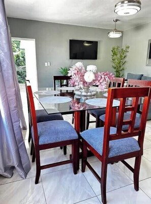A dining area with a glass table, wooden chairs, and a vase of flowers. - Nice two-bedroom apartment (Sosúa)