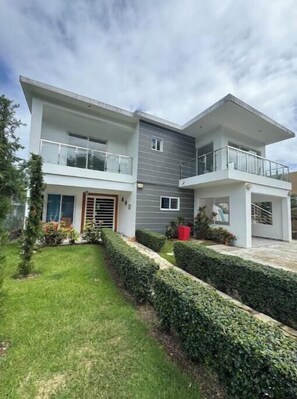 A modern two-story house with a balcony, a well-maintained lawn, and a small garden area. - Nice two-bedroom apartment (Sosúa)