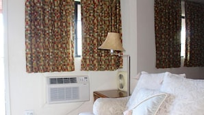 A bedroom with a bed, a lamp, an air conditioning unit, and curtains. - Starlite Motel (Mesa)