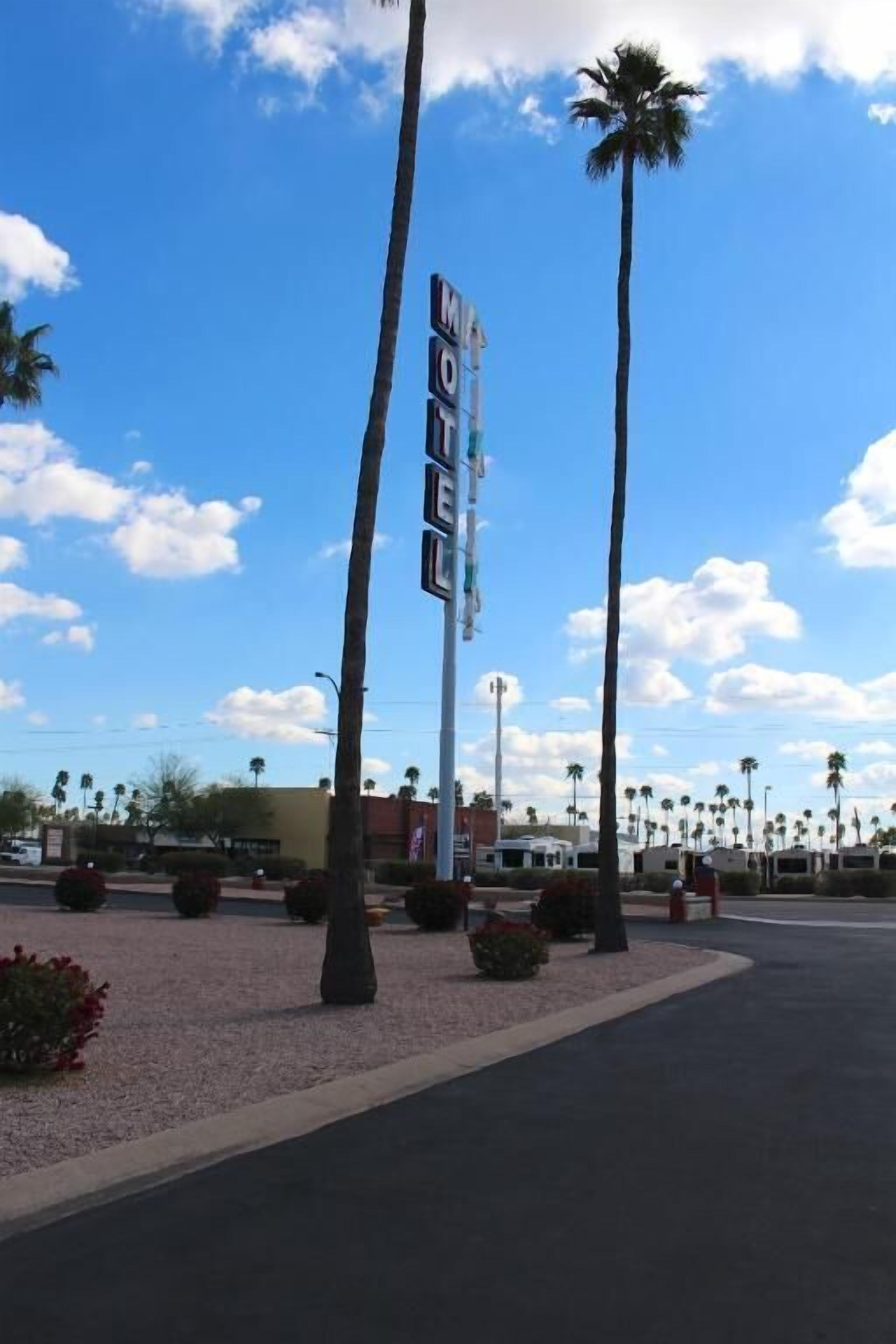 A motel sign with palm trees and a clear sky.