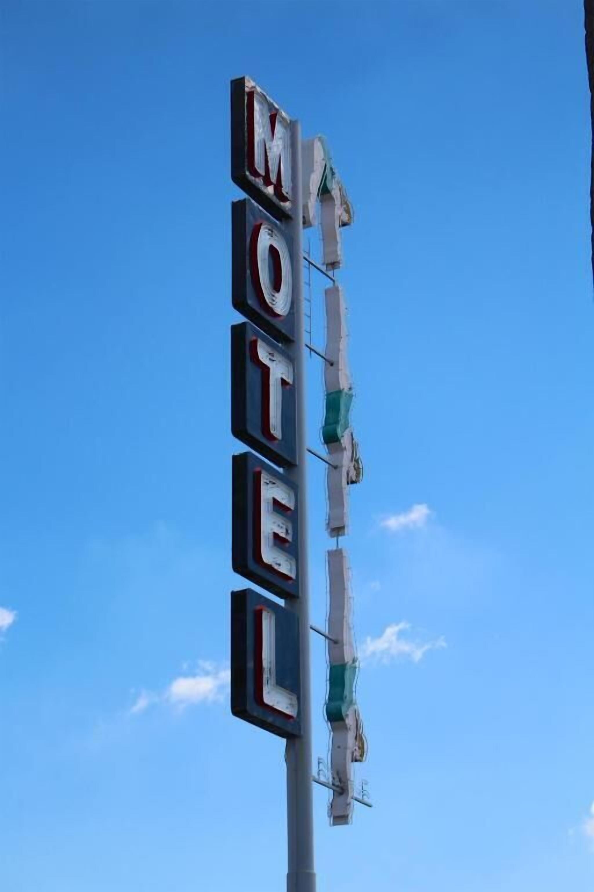 Un letrero de motel con el nombre 'MOTEL' y una señal de neón verde encima.