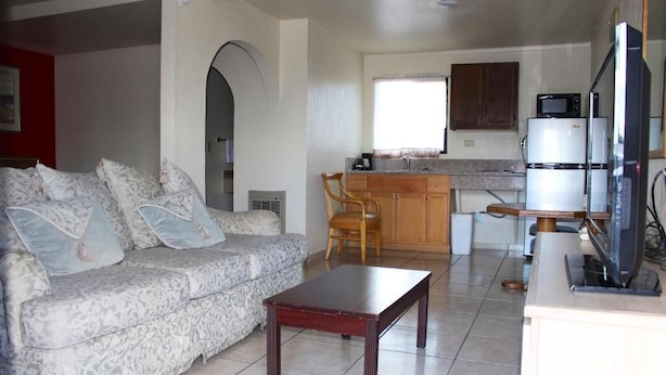 A living room with a sofa, a coffee table, and a kitchen area with a refrigerator and microwave. - Starlite Motel (Mesa)