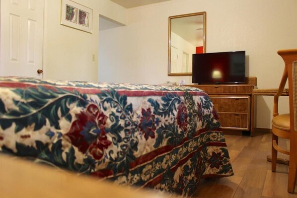 A bedroom with a bed, a television on a wooden dresser, a chair, and a mirror on the wall.