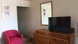 A room with a red chair, a wooden cabinet with a television, and a large mirror on the wall. - Starlite Motel (Mesa)