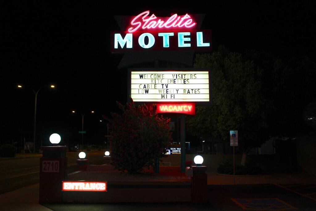 Een motelbord met neonverlichting, waarop 'Starlite MOTEL' staat, en een prikbord met advertenties voor kabeltelevisie, lage WiFi-tarieven en kamers beschikbaar.