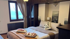 Une chambre à coucher avec un lit, un plancher en bois, une fenêtre avec des rideaux, un luminaire au plafond et un tableau accroché au mur.