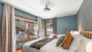 Une chambre avec un grand lit, deux fenêtres, un ventilateur de plafond et un mur décoré d’un motif.