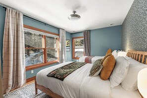 A bedroom with a large bed, two windows, a ceiling fan, and a patterned wall.