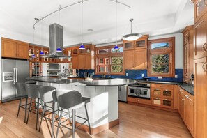 A modern kitchen with a central island, bar stools, wooden cabinets, and pendant lighting.