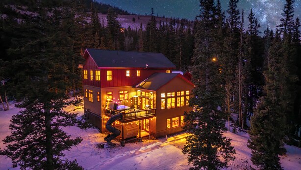 Une cabane dotée d’une grande terrasse, de nombreuses fenêtres et entourée d’un paysage enneigé.