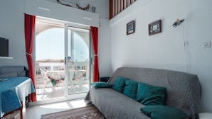 A room with a grey sofa, red curtains, a wooden table, and a patterned rug. - Serene Port-side Living in Agde (Agde)