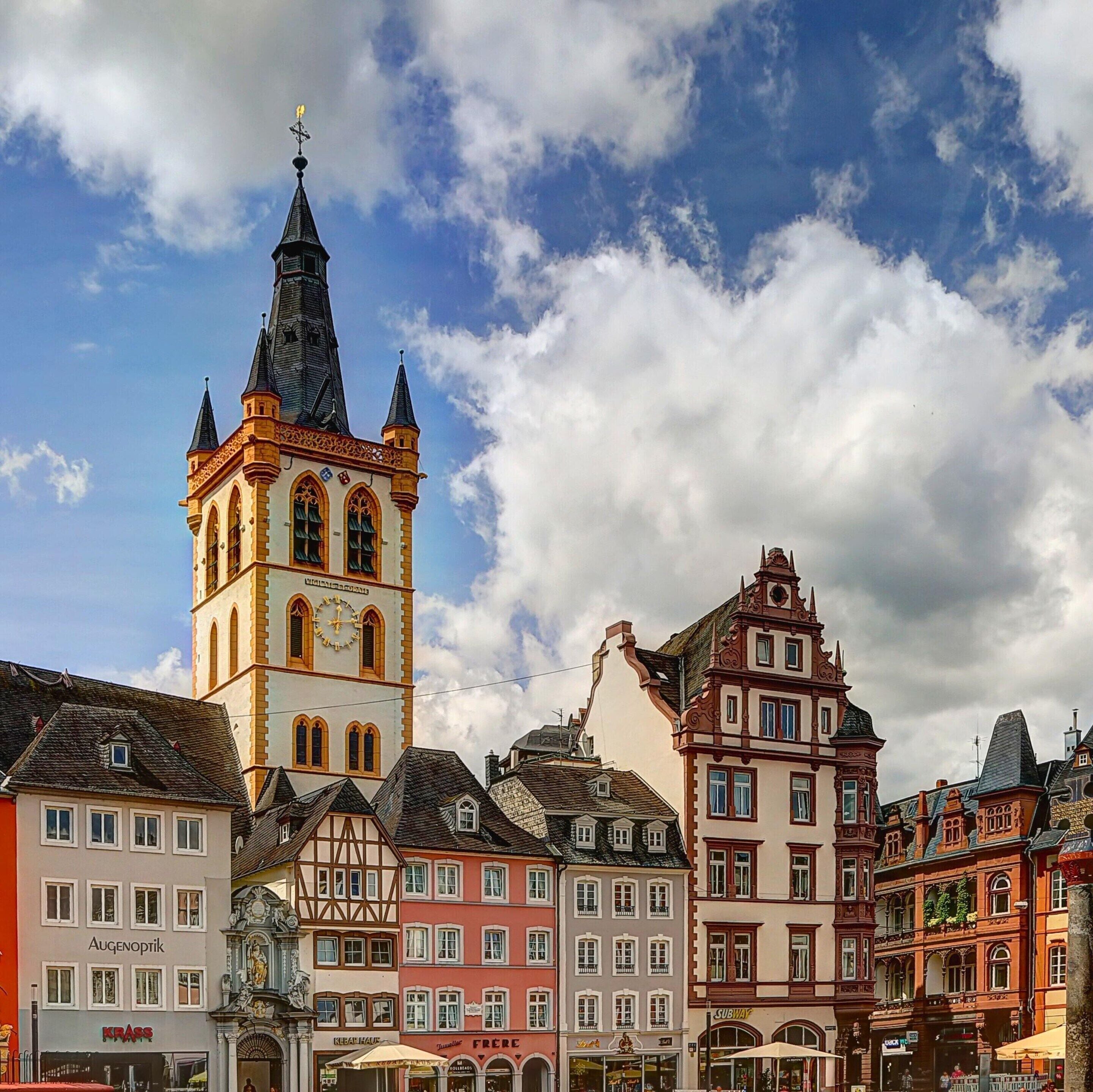 A historic building with a clock tower, adjacent traditional European architecture, and a clear sky.