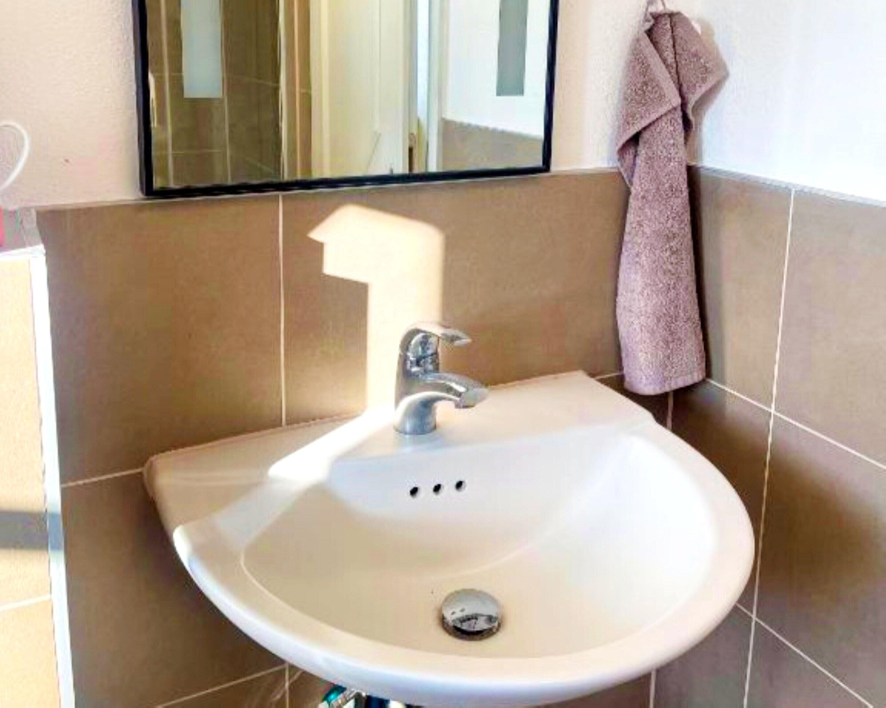 Une salle de bain avec un lavabo blanc, un miroir au-dessus et une serviette accrochée au mur.