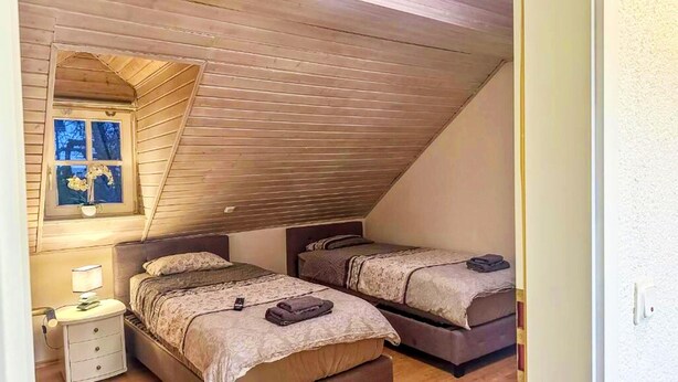 A bedroom with two beds, a nightstand, a window with a view, and a sloped ceiling. - Gemutliche Wohnung in Konz an der Mosel (Konz)