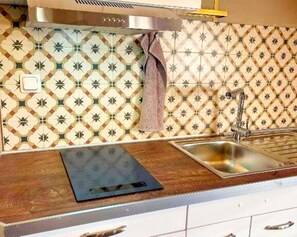A kitchen with patterned tiles, a stainless steel sink, and a wooden countertop.