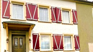 A two-story building with a green door, red shutters, and a small porch. - Gemutliche Wohnung in Konz an der Mosel (Konz)