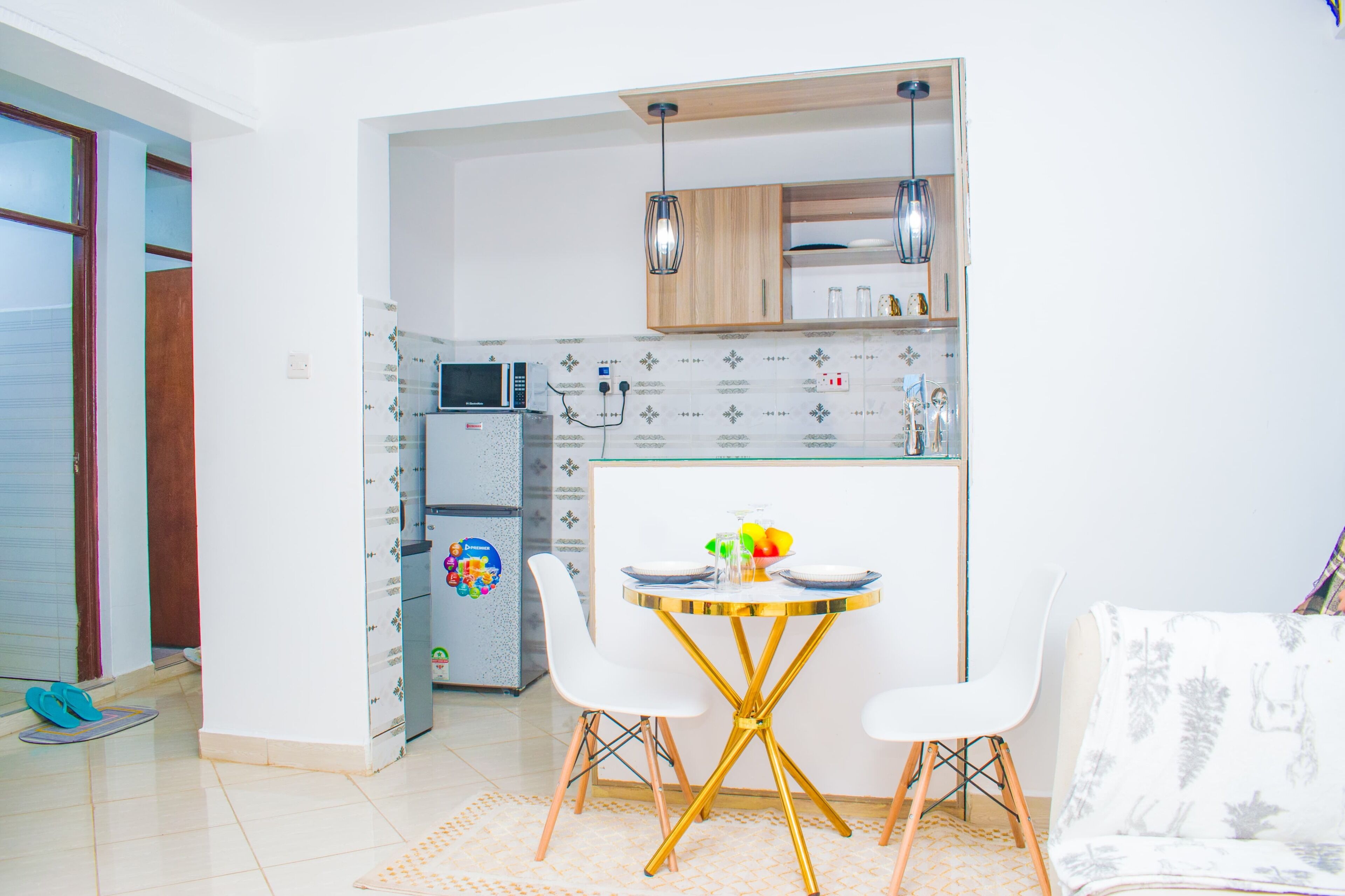 A compact kitchen with a microwave, refrigerator, and wooden cabinets. There is a dining table with chairs and a small island with a glass top.