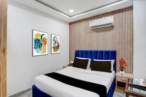 Camera d'albergo con un letto, due opere d'arte a parete, un comodino, un telefono, un vaso con fiori e un condizionatore d'aria.