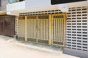Una entrada cerrada con un portón metálico, un camino de hormigón y un muro blanco con diseño decorativo.