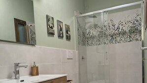Une salle de bain avec un meuble-lavabo en bois, deux toilettes, une douche avec une porte en verre et un miroir au-dessus du meuble-lavabo.