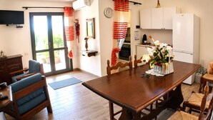 A dining area with a wooden table, chairs, a television, a refrigerator, and a window with curtains. - Terraced house with private garden Costa Rei, 300 meters from the sandy beach. (Costa Rei)