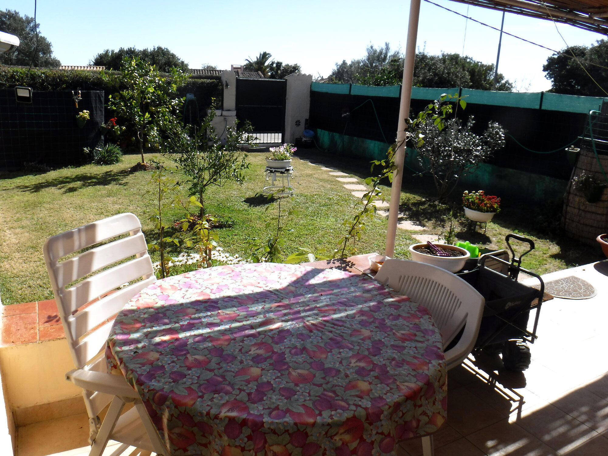 A patio with a table and chairs, surrounded by a garden and a fenced area.