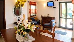 A living room with a wooden dining table, a sofa, a television, and a window with curtains. - Terraced house with private garden Costa Rei, 300 meters from the sandy beach. (Costa Rei)