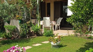 A well-maintained garden with a flamingo sculpture, a patio area with chairs, and a building with a tiled roof. - Terraced house with private garden Costa Rei, 300 meters from the sandy beach. (Costa Rei)