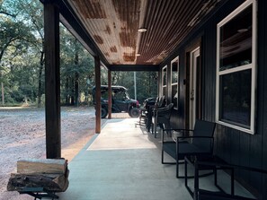 A covered outdoor seating area with a concrete floor, wooden posts, and a row of chairs. - Wild Ride Retreat near Albert Pike & Caddo River trailer parking Pets allowed (Caddo Gap)