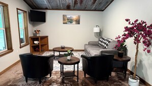 A living room with a sofa, two armchairs, a coffee table, a TV, a painting, a lamp, a potted plant, and a window with a view. - Wild Ride Retreat near Albert Pike Caddo River ATV trailer parking Pets allowed (Caddo Gap)