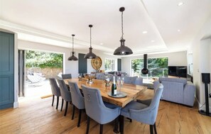A dining area with a wooden table, blue chairs, and pendant lights. - Luxury Sea View Home with Hot Tub & Sauna (Llanallgo)