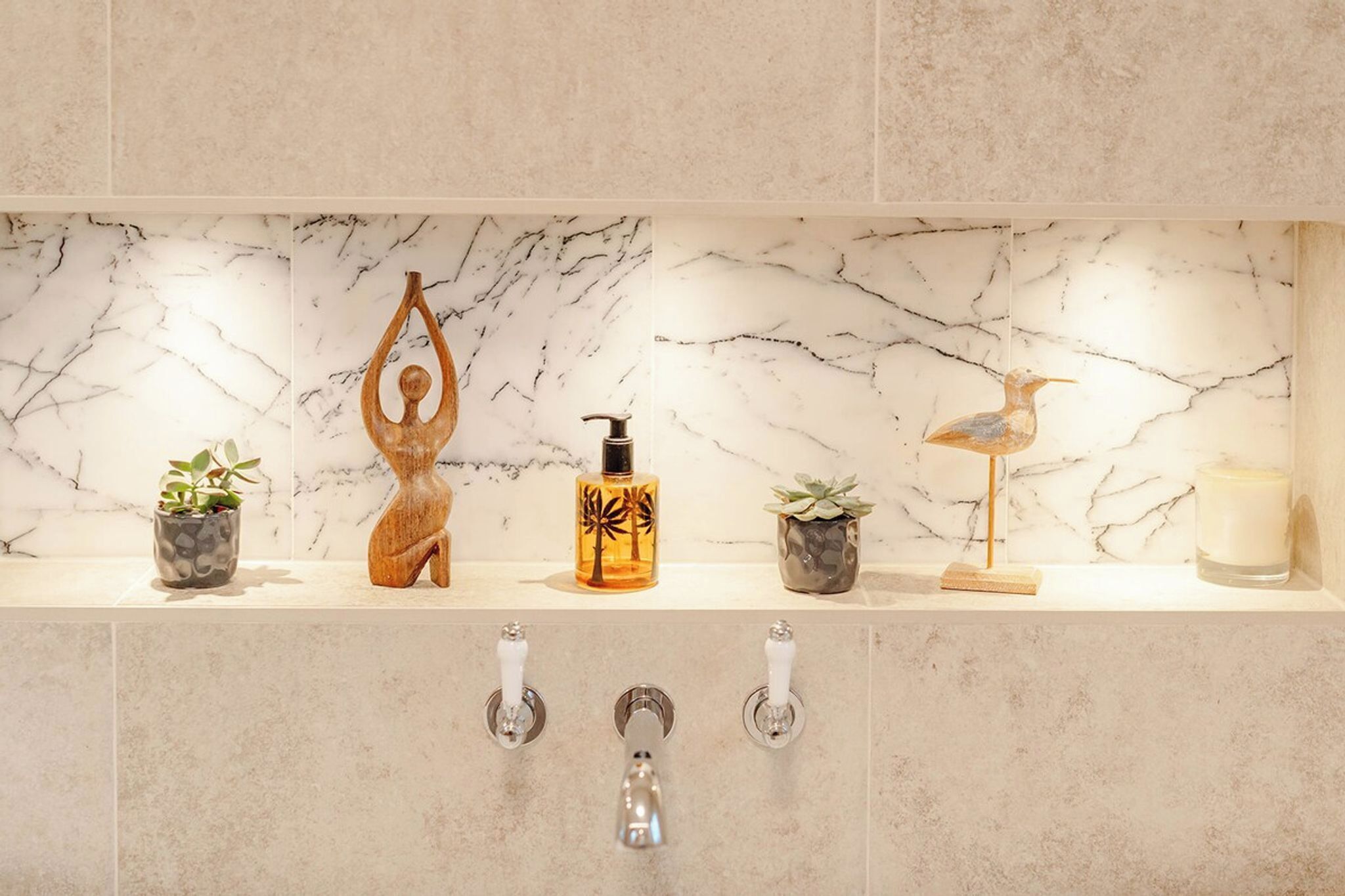 A bathroom vanity with a marble backsplash, a wooden sculpture, a bottle with a palm tree design, a small bird sculpture, and a candle.