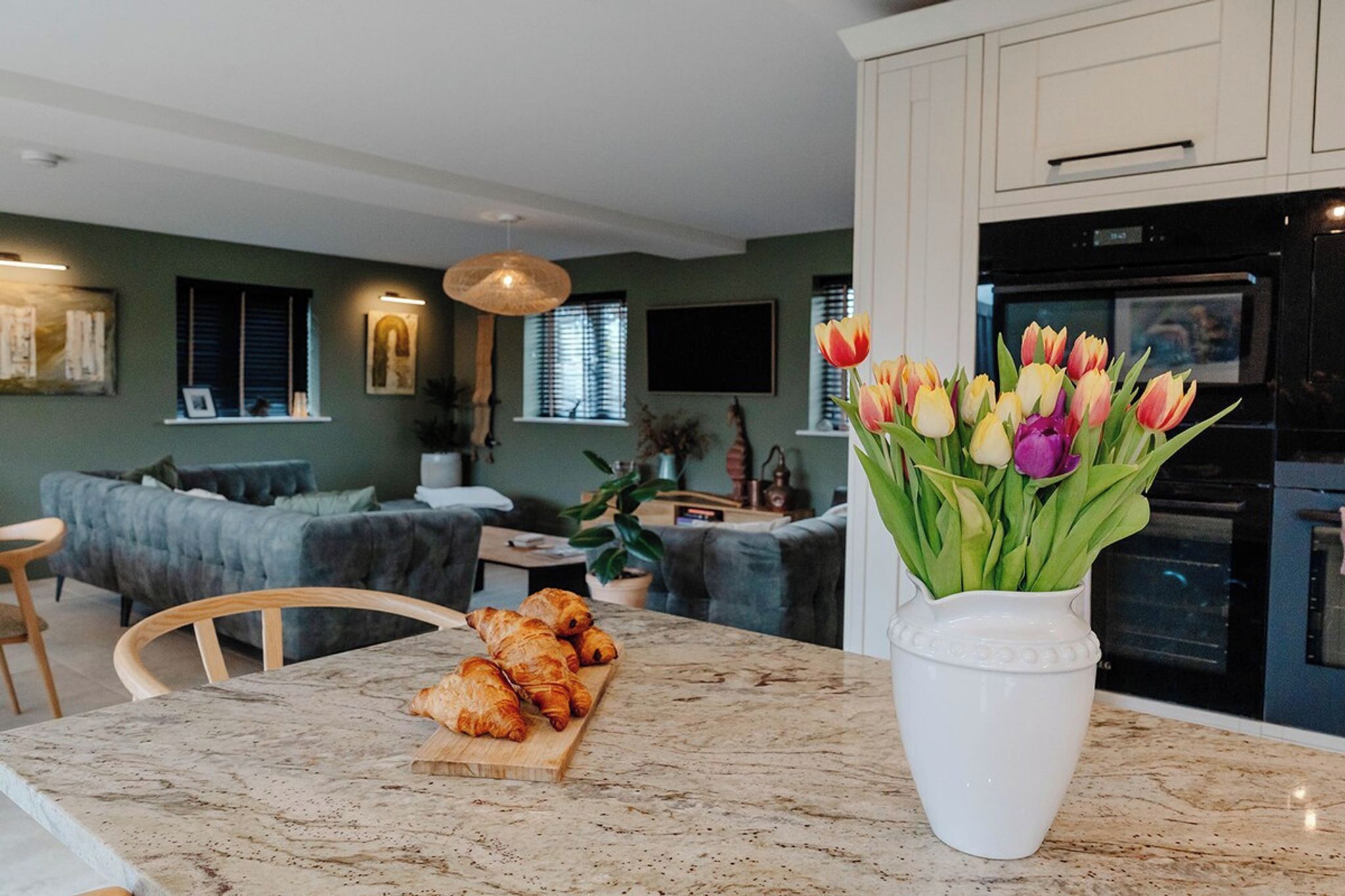 A modern kitchen with a marble countertop, a dining area with a table and chairs, and a living room with a sofa and a TV.