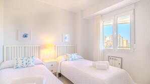 Une chambre d’hôtel avec deux lits, du linge de lit blanc, un radiateur, une fenêtre avec des rideaux et des œuvres d’art accrochées au mur.