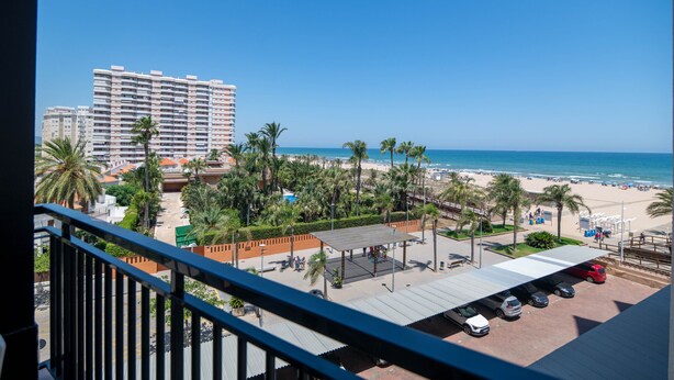 Un hôtel de grande hauteur offrant une vue sur la plage, avec un espace de stationnement et un espace extérieur couvert aménagé en coin salon.