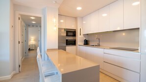 Une cuisine moderne avec des meubles blancs, un îlot central, un four encastré et une machine à café.