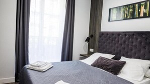 Una cama bien tendida con una colcha gris, un cabecero oscuro y una almohada.