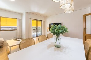 A modern dining area with a large table, wicker chairs, a vase with greenery, and a TV on the wall. - New lovely apartment in front of the beach - only families (Playa de Gandía)