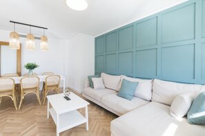 A modern living room with a white sofa, a dining table with chairs, and a blue accent wall. - New lovely apartment in front of the beach - only families (Playa de Gandía)