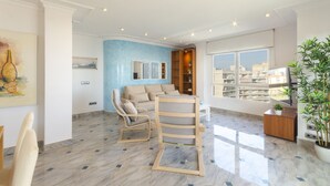 Uma sala de estar moderna com uma parede azul de destaque, um sofá, uma cadeira de madeira, uma mesa de centro e uma grande janela com vista para a cidade.