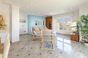 A modern living room with a blue accent wall, a sofa, a wooden chair, a coffee table, and a large window with a city view. - AG SALINAS 9 - only families (Playa de Gandía)